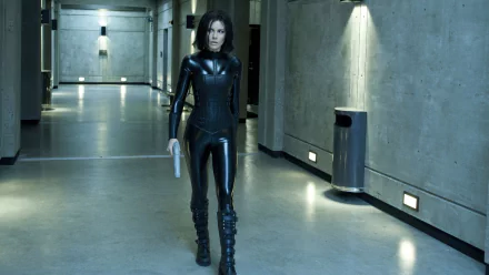 Kate Beckinsale portrays Selene in Underworld: Awakening, walking confidently through a dimly lit corridor, dressed in a sleek black outfit. HD wallpaper for fans of the film.