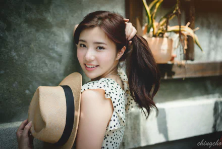 A smiling Taiwanese woman with long hair holds a hat, posing playfully against a textured background, capturing a vibrant and cheerful moment in 4K Ultra HD.