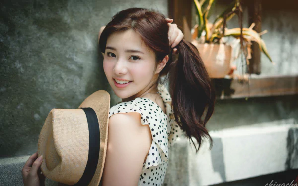 A smiling Taiwanese woman with long hair holds a hat, posing playfully against a textured background, capturing a vibrant and cheerful moment in 4K Ultra HD.