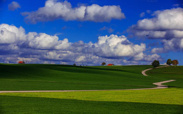 A winding road through vibrant green countryside under a sky filled with fluffy clouds, captured in stunning 4K Ultra HD landscape photography.