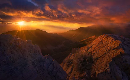 HD desktop wallpaper showcasing a dramatic mountain landscape bathed in golden sunbeams cutting through vibrant clouds at sunset.