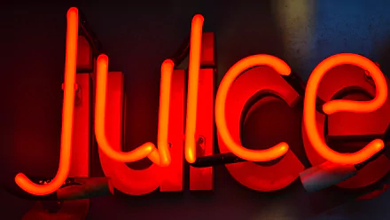 Vibrant orange neon sign spelling juice glows against a dark background, creating a striking HD desktop wallpaper with a bold, colorful photographic style.