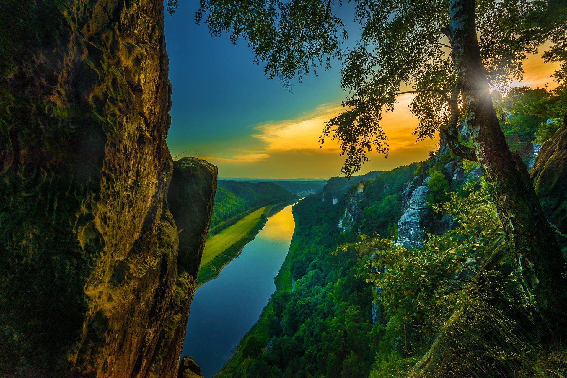 A serene sunrise casts golden light over a lush forest and winding river, framed by towering trees and rocky cliffs, showcasing the beauty of nature's landscape.