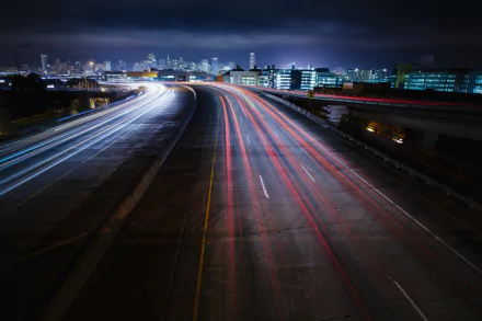 A time-lapse photograph of a highway in San Francisco, California, showcasing dynamic light trails against a city skyline at night. HD wallpaper for desktop backgrounds.