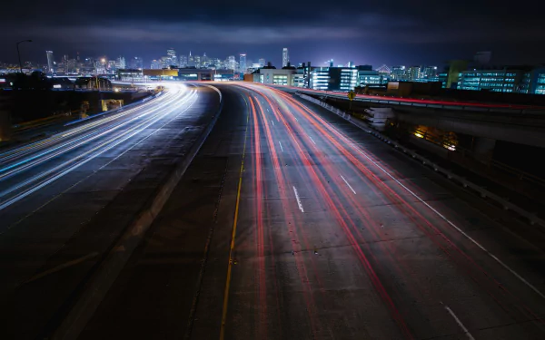 A time-lapse photograph of a highway in San Francisco, California, showcasing dynamic light trails against a city skyline at night. HD wallpaper for desktop backgrounds.