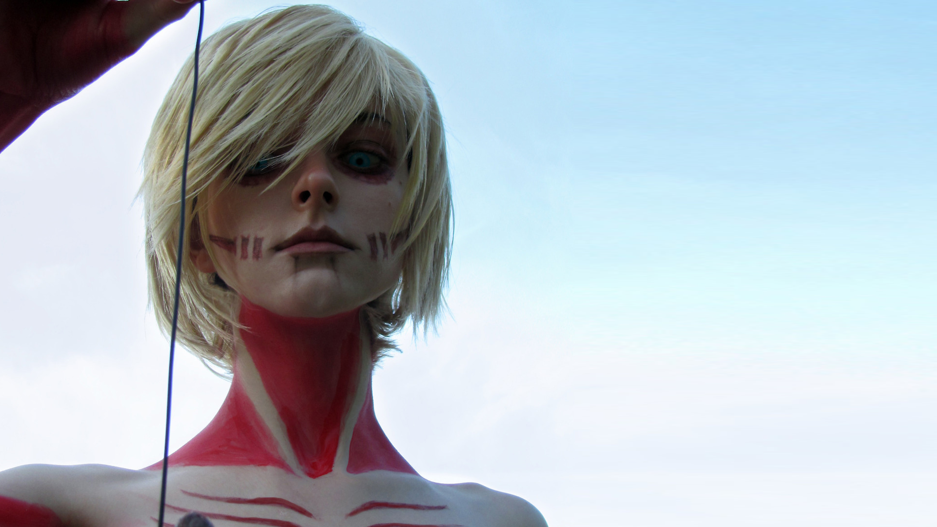 HD PC desktop wallpaper featuring a woman in detailed Attack on Titan cosplay with painted skin and blonde hair against a clear sky background.