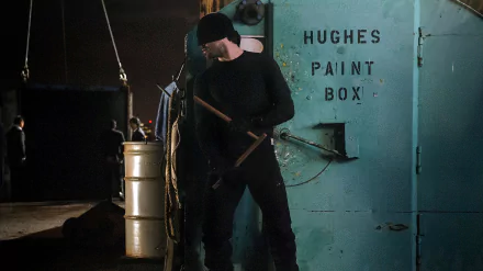Daredevil (TV show) 2K Quad HD PC desktop wallpaper: shadowy figure in black and beanie holding batons beside a metal door labeled Hughes Paint Box in a dim industrial dock setting.
