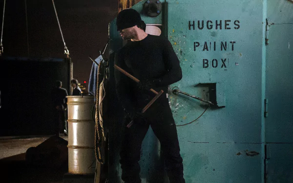 Daredevil (TV show) 2K Quad HD PC desktop wallpaper: shadowy figure in black and beanie holding batons beside a metal door labeled Hughes Paint Box in a dim industrial dock setting.