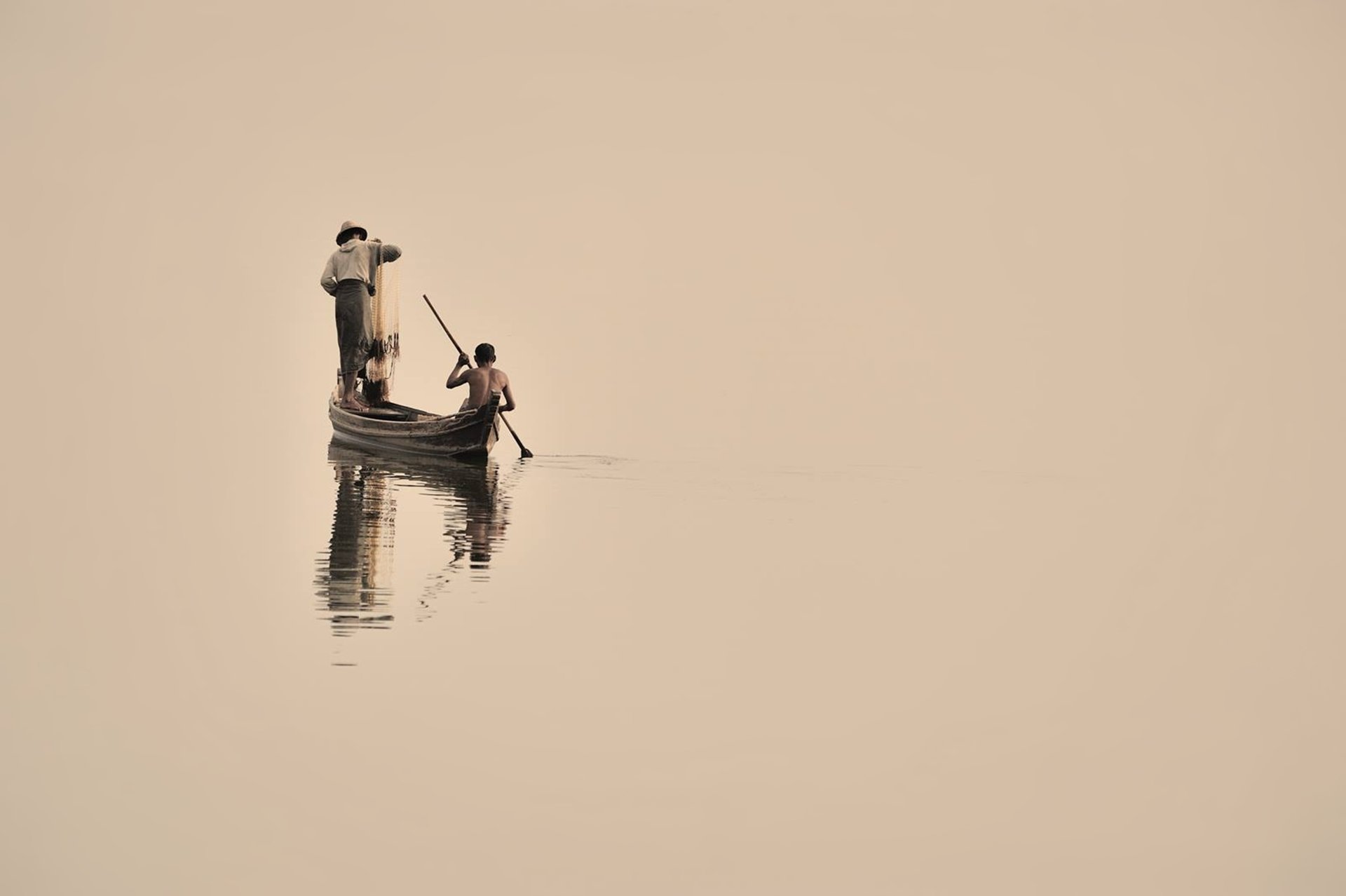 A serene HD wallpaper featuring fishermen in a boat on a calm lake, their reflections visible in the water, capturing the tranquility of outdoor fishing life.
