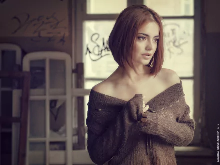 HD desktop wallpaper of a redhead woman with brown eyes, wearing an off-shoulder sweater, posing thoughtfully in a softly lit indoor setting.