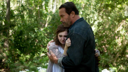 Still from the movie Maggie (2015) showing a man and young woman embracing in a lush forest, presented as a 4K Ultra HD PC desktop wallpaper and background.