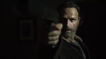 A dramatic HD wallpaper from the TV show The Walking Dead features a close-up of a rugged character aiming a weapon, set against a dark backdrop.