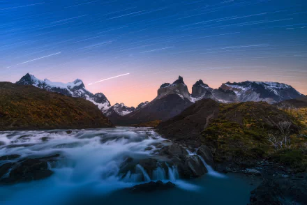 Time-lapse stars streak over the rugged mountains of Torres del Paine, Chile, with a flowing river under a night sky in Patagonia’s stunning natural landscape.