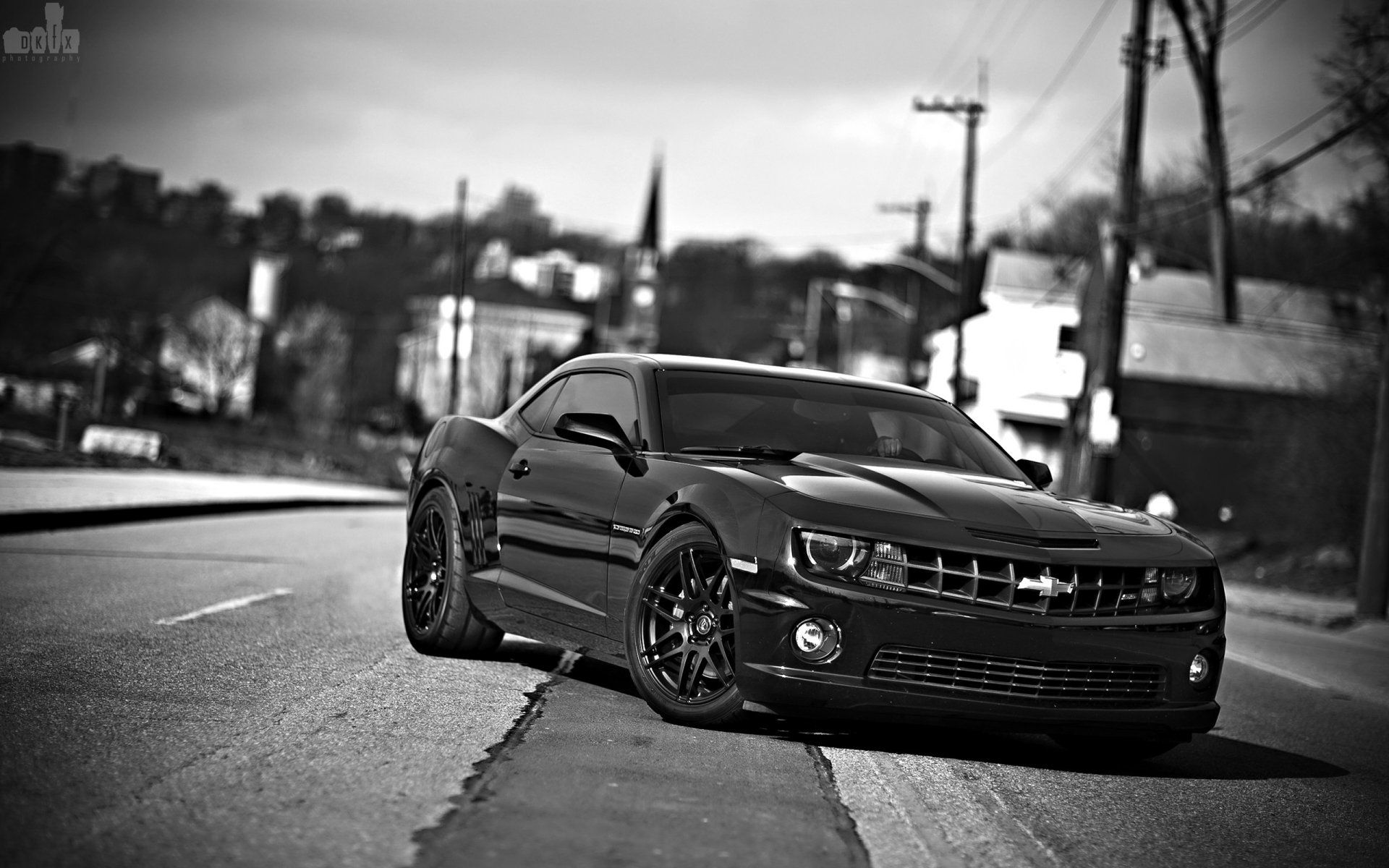 Black-and-white 2K Quad HD PC desktop wallpaper of a Chevrolet Camaro parked on an urban street, low-angle perspective emphasizing its aggressive stance.