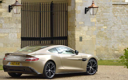 2K Quad HD PC desktop wallpaper and background: Aston Martin vehicle in champagne parked by a stone manor, rear three-quarter view highlighting sleek curves and alloy wheels.