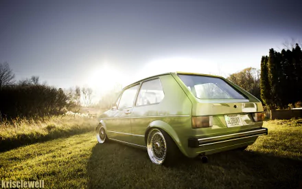 Green Volkswagen Golf Mk1 parked on sunlit grass at sunset, low-angle HD PC desktop wallpaper and background.