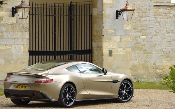 2K Quad HD PC desktop wallpaper and background: Aston Martin vehicle in champagne parked by a stone manor, rear three-quarter view highlighting sleek curves and alloy wheels.
