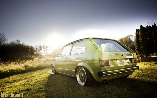 Green Volkswagen Golf Mk1 parked on sunlit grass at sunset, low-angle HD PC desktop wallpaper and background.