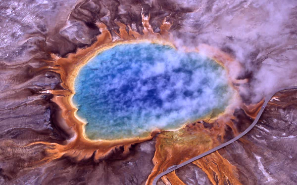 Aerial HD photograph of Yellowstone’s Grand Prismatic Spring in spring, showcasing vibrant blue, orange, and brown mineral-rich waters and surrounding landscape.