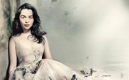 A striking HD desktop wallpaper featuring celebrity Emilia Clarke, elegantly posed in a floral dress, set against a softly blurred background.