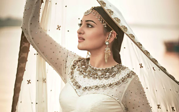 HD desktop wallpaper featuring celebrity Sonakshi Sinha, adorned in an elegant outfit with intricate jewelry, gazing into the distance against a serene outdoor background.