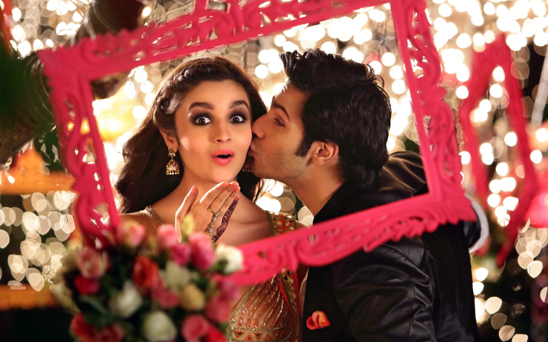 HD desktop wallpaper featuring Varun Dhawan kissing Alia Bhatt on the cheek, from the movie Humpty Sharma Ki Dulhania. The image captures a playful and romantic moment adorned with vibrant decorations.
