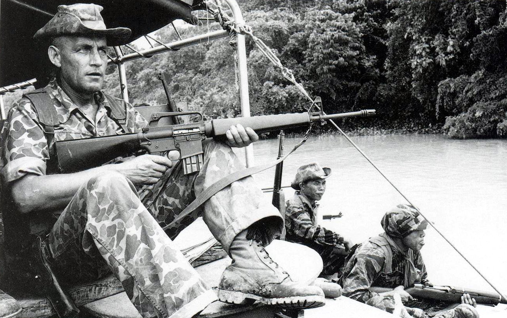 Black and white Vietnam War military scene shows soldiers armed and alert on a boat navigating a river, captured in an HD PC desktop wallpaper and background.