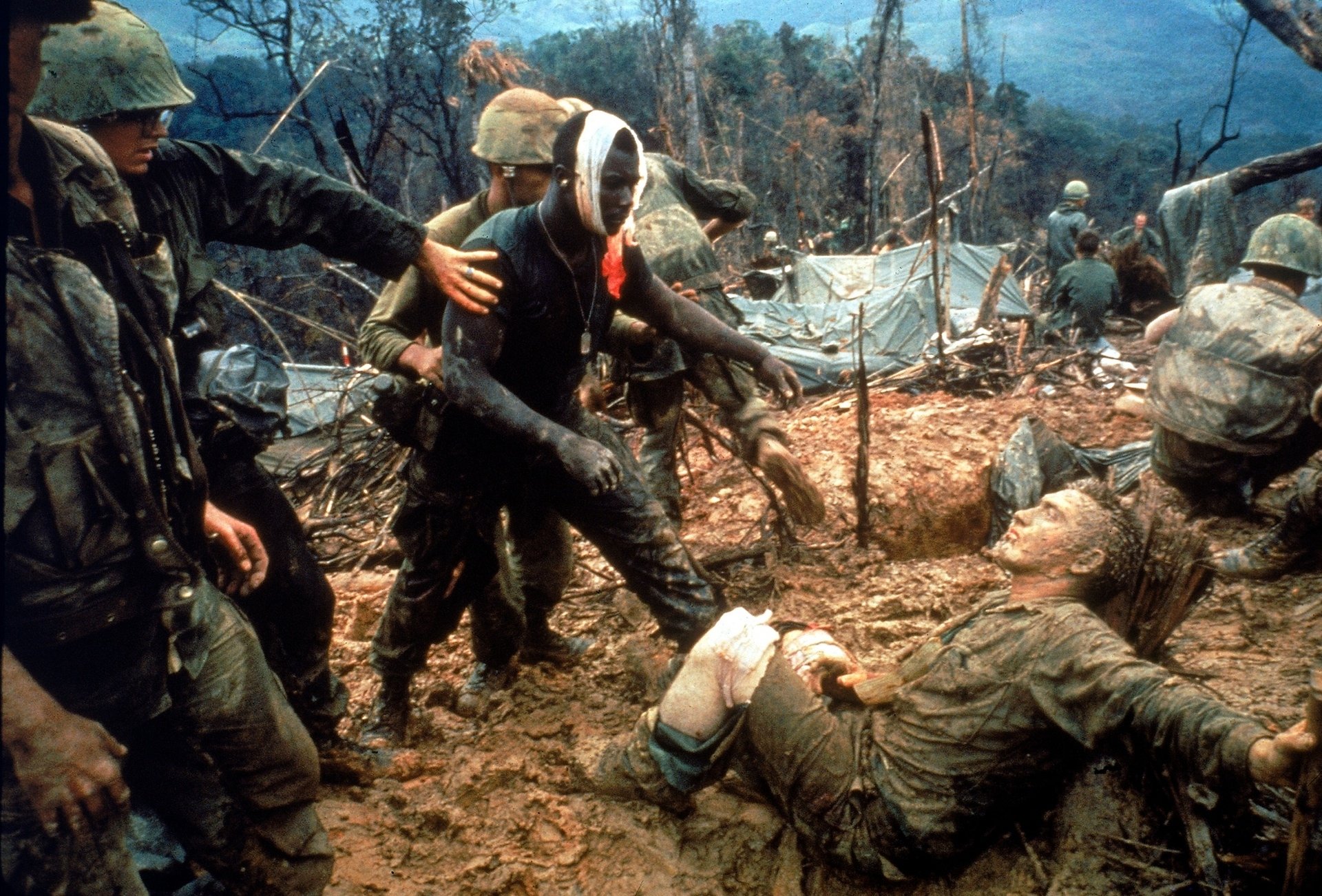 Vietnam War military scene showing soldiers aiding a wounded comrade in a muddy, forested battlefield, captured in high-definition for a PC desktop wallpaper.
