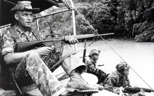 Black and white Vietnam War military scene shows soldiers armed and alert on a boat navigating a river, captured in an HD PC desktop wallpaper and background.