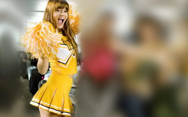 Smiling woman in yellow cheerleader uniform waving pom-poms, cinematic still labeled Death Proof — 2K Quad HD PC desktop wallpaper/background.