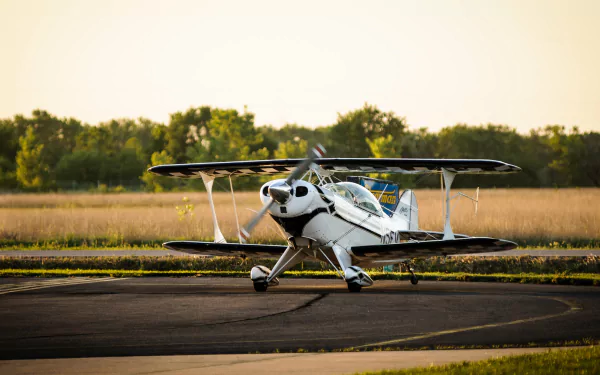 4K Ultra HD PC desktop wallpaper: white single-engine biplane (vehicle, aircraft) parked on a runway at sunset with grassy field and trees in the background.