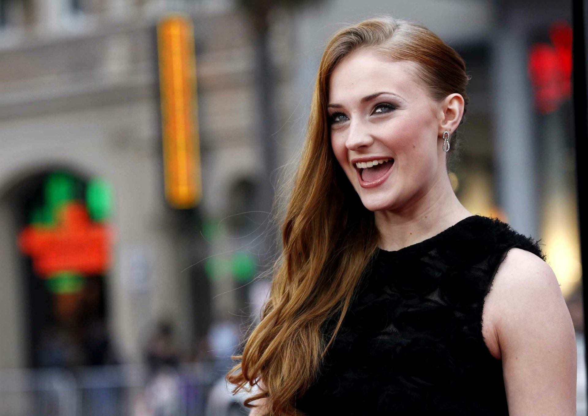 HD PC desktop wallpaper featuring celebrity Sophie Turner smiling outdoors with blurred city background.