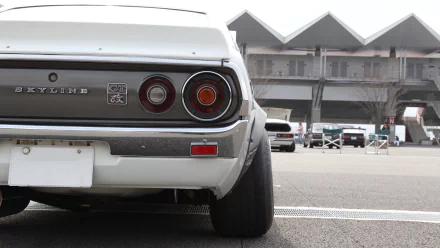 A Nissan Skyline parked with a focus on its rear, showcasing the iconic taillights against a backdrop of an automotive venue. HD desktop wallpaper and background.