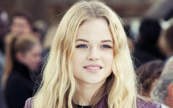 HD PC desktop wallpaper featuring a close-up portrait of woman Gabriella Wilde with long blonde hair and a soft smile, set against a blurred crowd background.