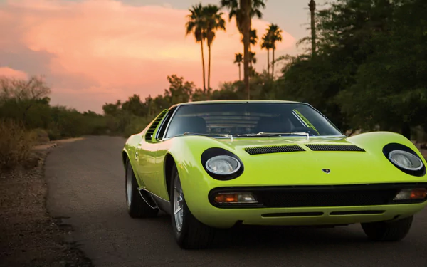 HD desktop wallpaper showcasing a vibrant yellow Lamborghini Miura parked on a scenic road at sunset with palm trees and lush greenery in the background.