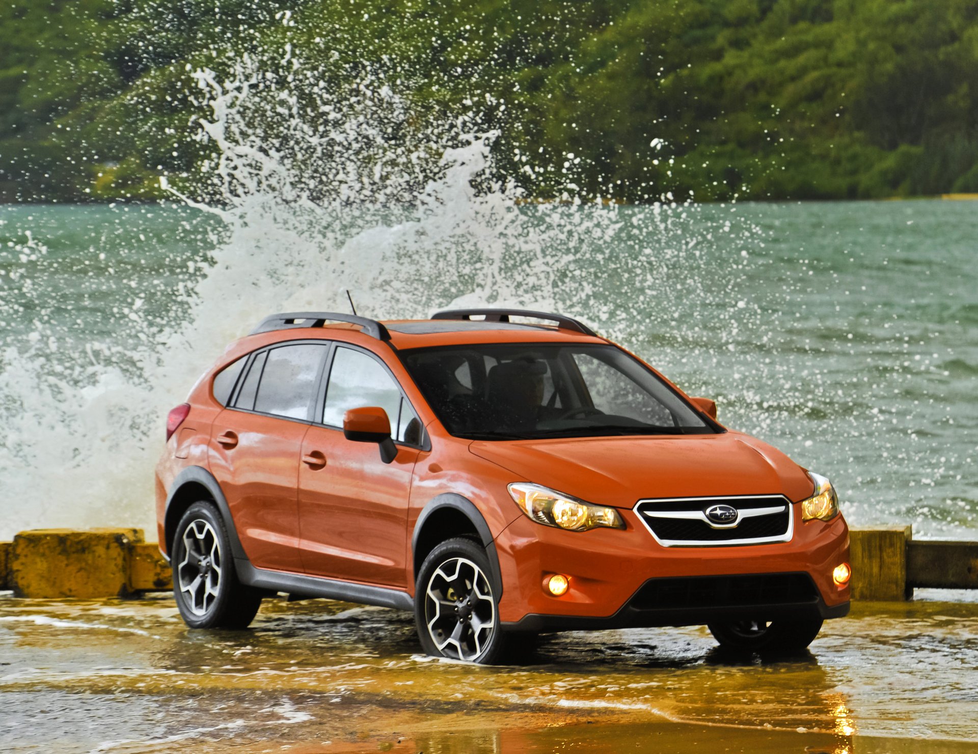 Subaru Crosstrek parked by water with waves splashing around, serving as a vibrant HD desktop wallpaper.