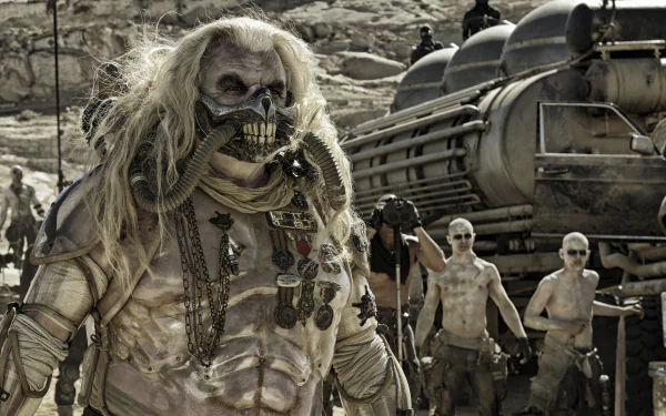 Immortan Joe, portrayed by Hugh Keays-Byrne in Mad Max: Fury Road, stands menacingly in a post-apocalyptic desert setting with his war boys in the background.