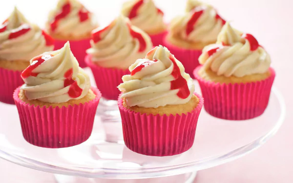 4K Ultra HD desktop wallpaper of cupcakes with creamy frosting and red drizzle in bright pink liners on a glass stand, highlighting delicious food details.