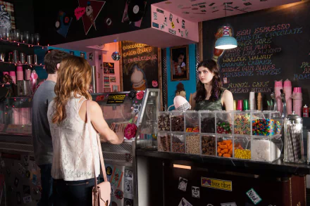 A scene from the movie Burying the Ex, featuring a vibrant ice cream shop with a customer at the counter and a server behind it, showcasing colorful candy options.
