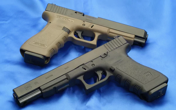 HD desktop wallpaper showcasing two Glock pistols against a blue fabric background. The pistols are displayed in a cross pattern, highlighting their design and details.