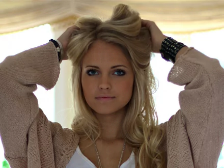 HD desktop wallpaper featuring a woman tagged as Emilie Marie Nereng, with a serene expression, holding her blonde hair up, in a softly lit, cozy indoor setting.