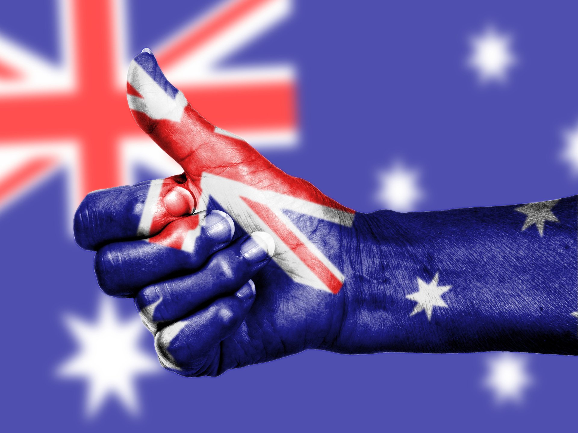 2K Quad HD PC desktop wallpaper: close-up of a hand painted with the Australian flag giving a thumbs-up against a blurred Australian flag background.