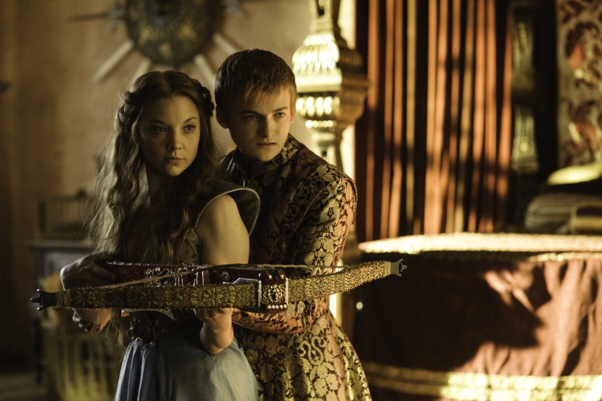 Jack Gleeson as Joffrey Baratheon stands behind Natalie Dormer as Margaery Tyrell in a dramatic scene from the TV show Game of Thrones, shown in HD desktop wallpaper quality.