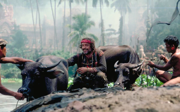 A captivating HD desktop wallpaper from *Apocalypse Now*, featuring a man interacting with water buffalo in a lush, tropical setting, surrounded by palm trees and mist.