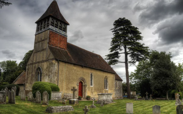 Religious church 4K Ultra HD PC desktop wallpaper: historic stone church with red door, surrounding graveyard and a tall tree beneath a dramatic cloudy sky.