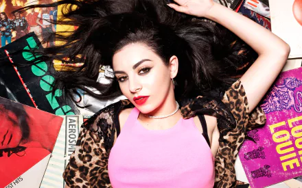 HD PC desktop wallpaper featuring Charli XCX lying among colorful music albums and posters, blending vibrant visual elements with a bold pop music vibe.