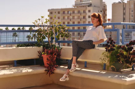 A woman, Alina Kovalenko, sitting on a sunlit terrace with plants around, while urban buildings rise in the background.