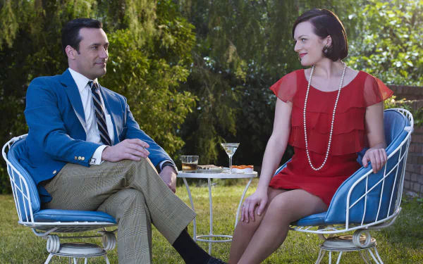 Mad Men TV show 2K Quad HD PC desktop wallpaper: two characters seated in retro patio chairs, man in blue suit and woman in red dress chatting over cocktails in a sunlit garden.