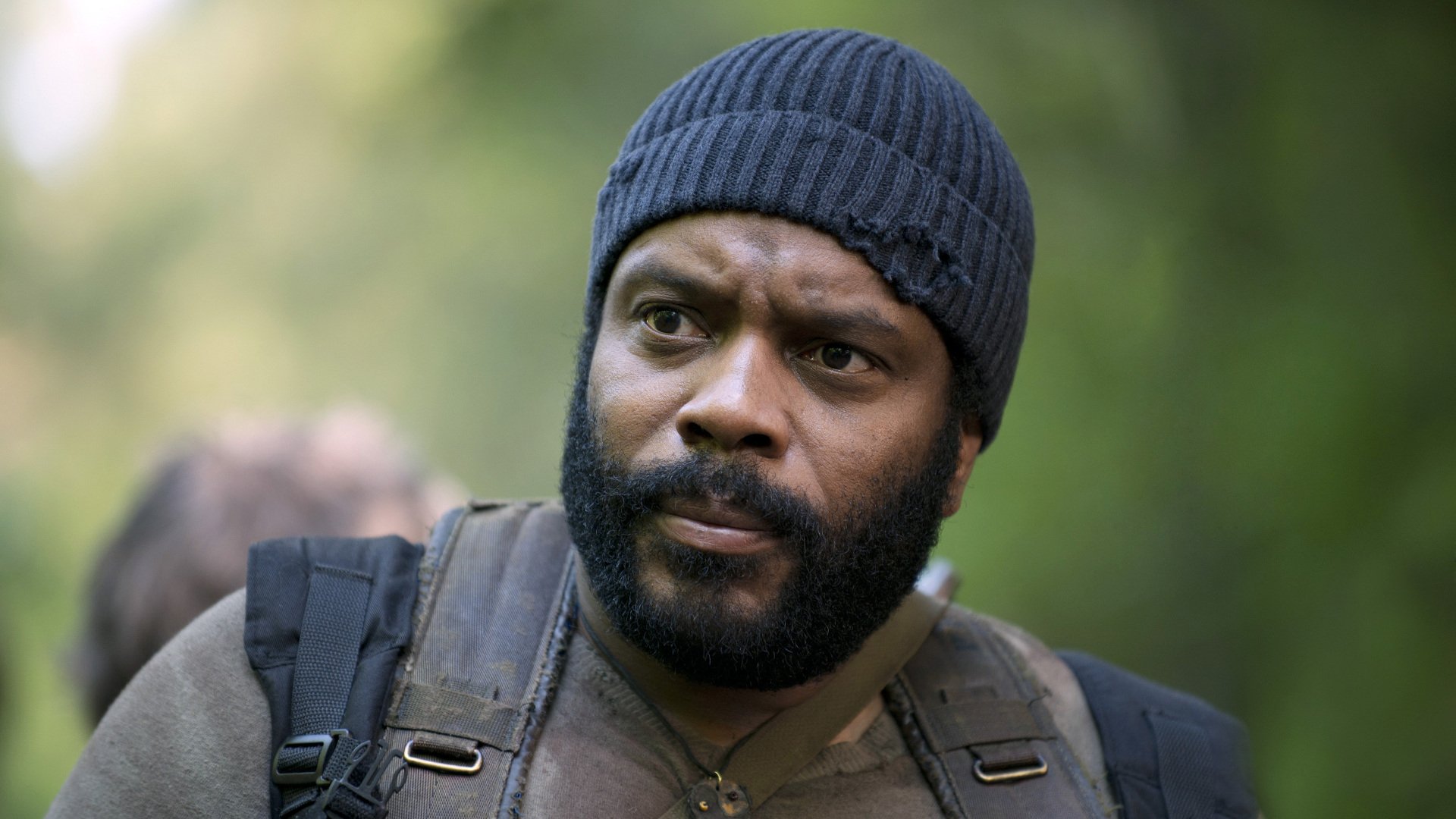 HD PC desktop wallpaper of a bearded man in a knit cap and backpack in a wooded scene from the TV show The Walking Dead.