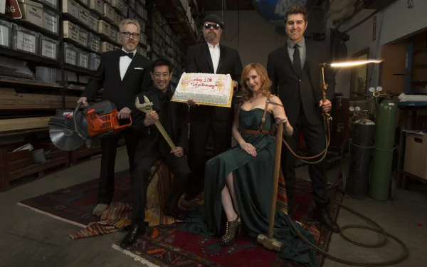HD PC desktop wallpaper/background: MythBusters TV show workshop scene — five people in formal wear posed amid tools, a cake and experimental gear.